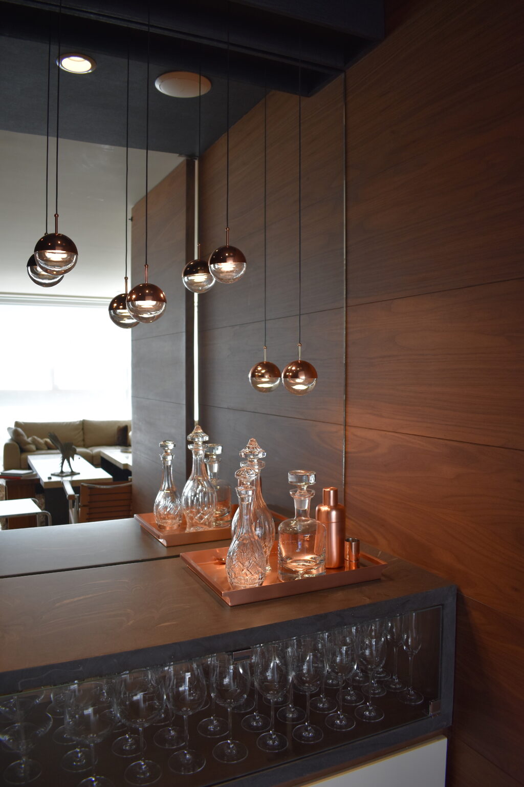 Bar con decantadores de cristal, lámparas esféricas y espejo hacia la sala