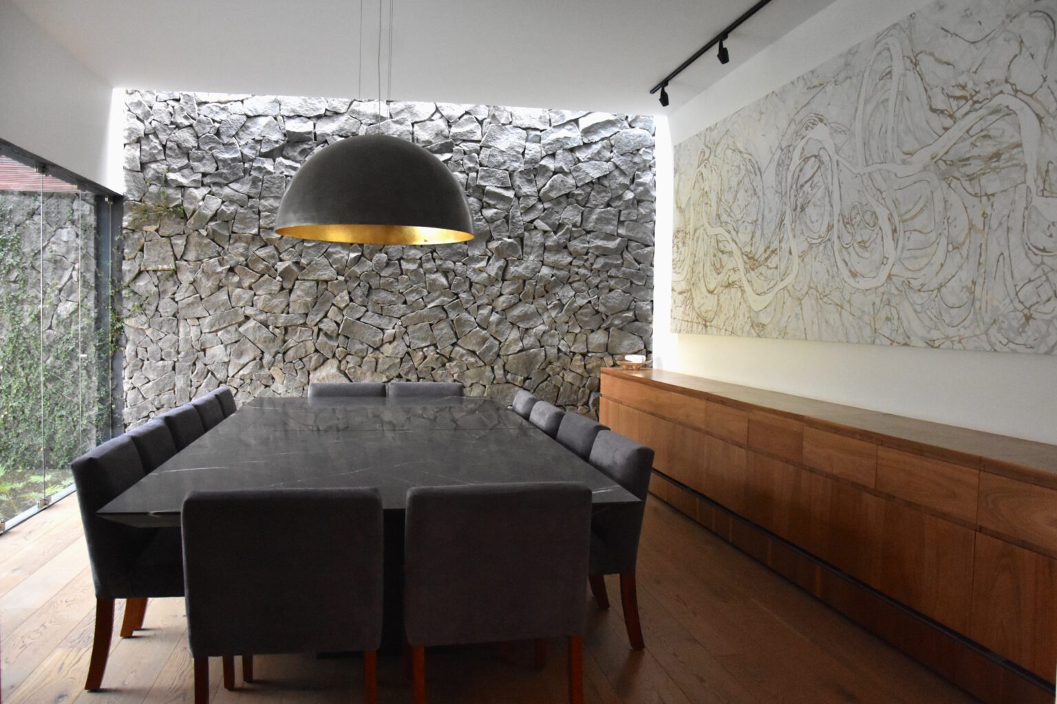 Comedor de Bosques 83 con mesa negra, lámpara colgante y muro de piedra