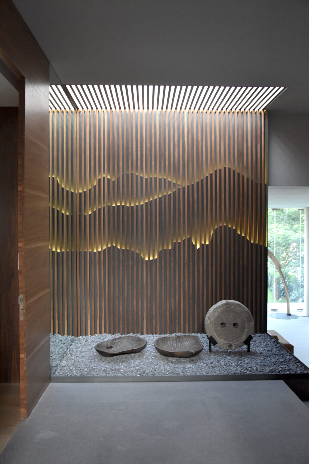 Vestíbulo de Bosques 83 con celosía de madera iluminada y jardín de piedra
