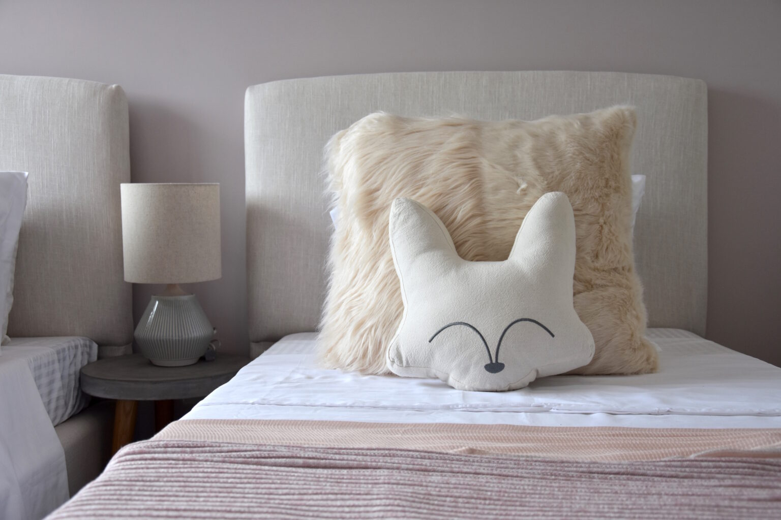 Detalle de cama infantil con cabecera tapizada y cojines de peluche en Real de Monteza
