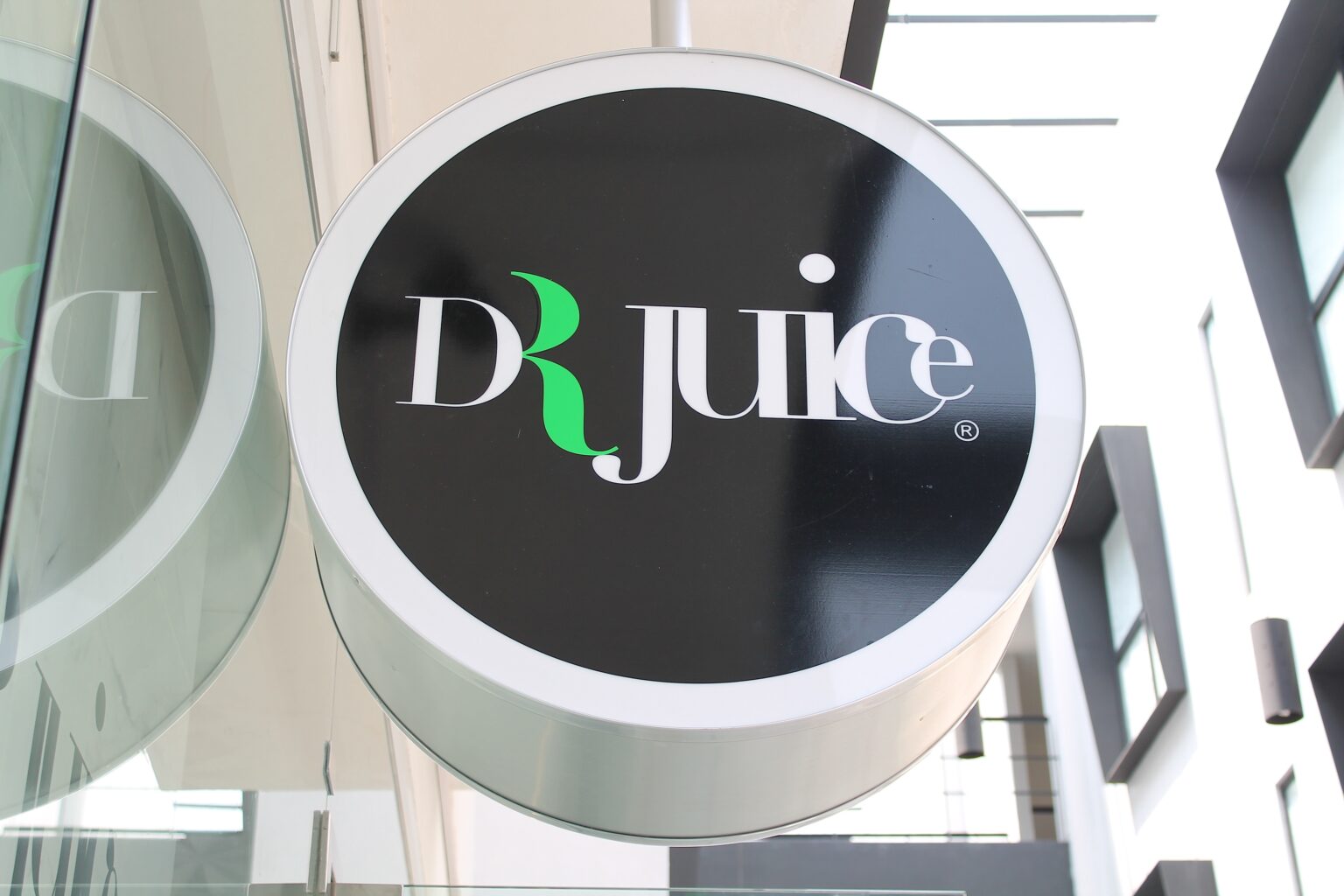 Rótulo circular exterior de Dr. Juice instalado sobre la fachada de cristal