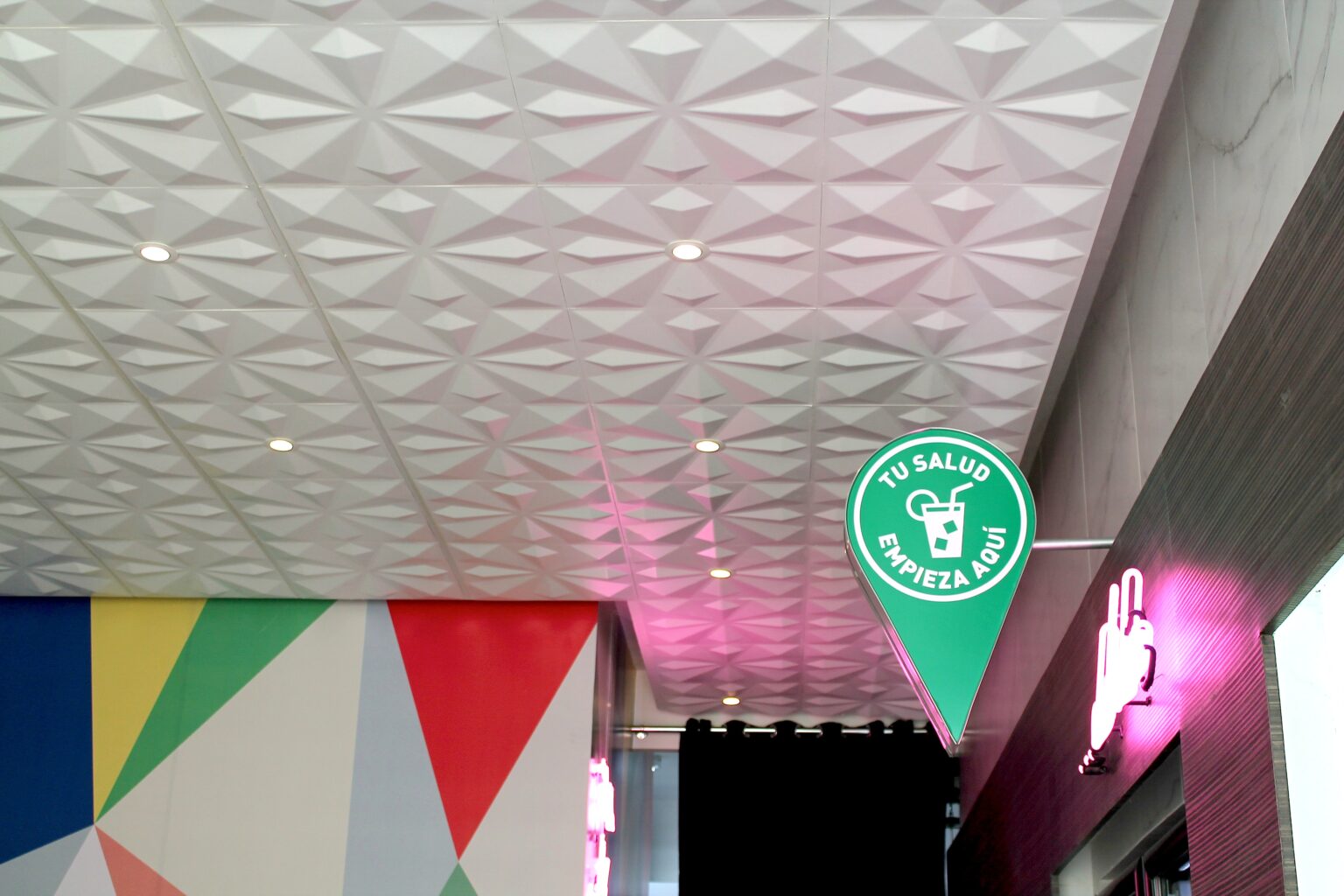 Plafón tridimensional con iluminación rosa, mural de colores y señal Tu salud empieza aquí
