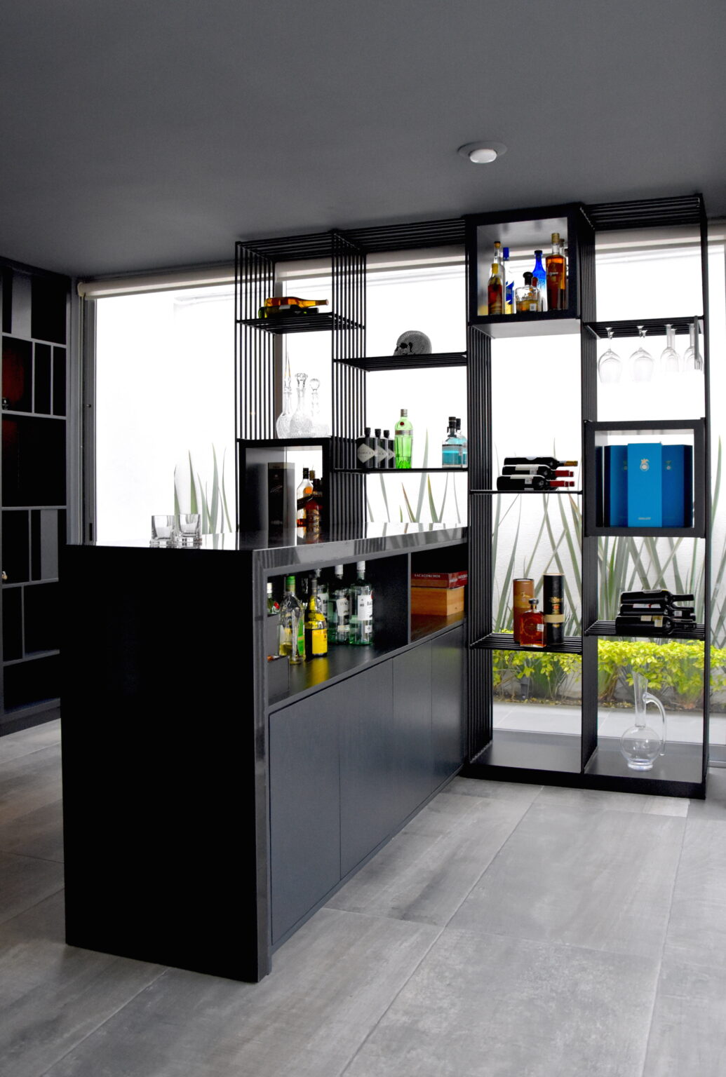 Mueble bar negro con almacenamiento y estantería metálica junto a los ventanales