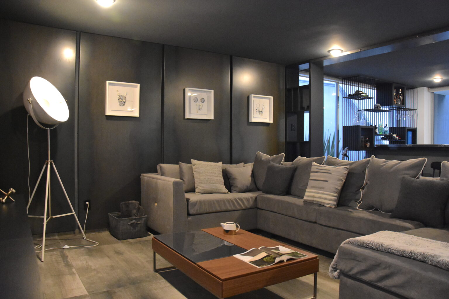 Sala familiar con sofá seccional gris, lámpara de trípode y mesa de centro de madera