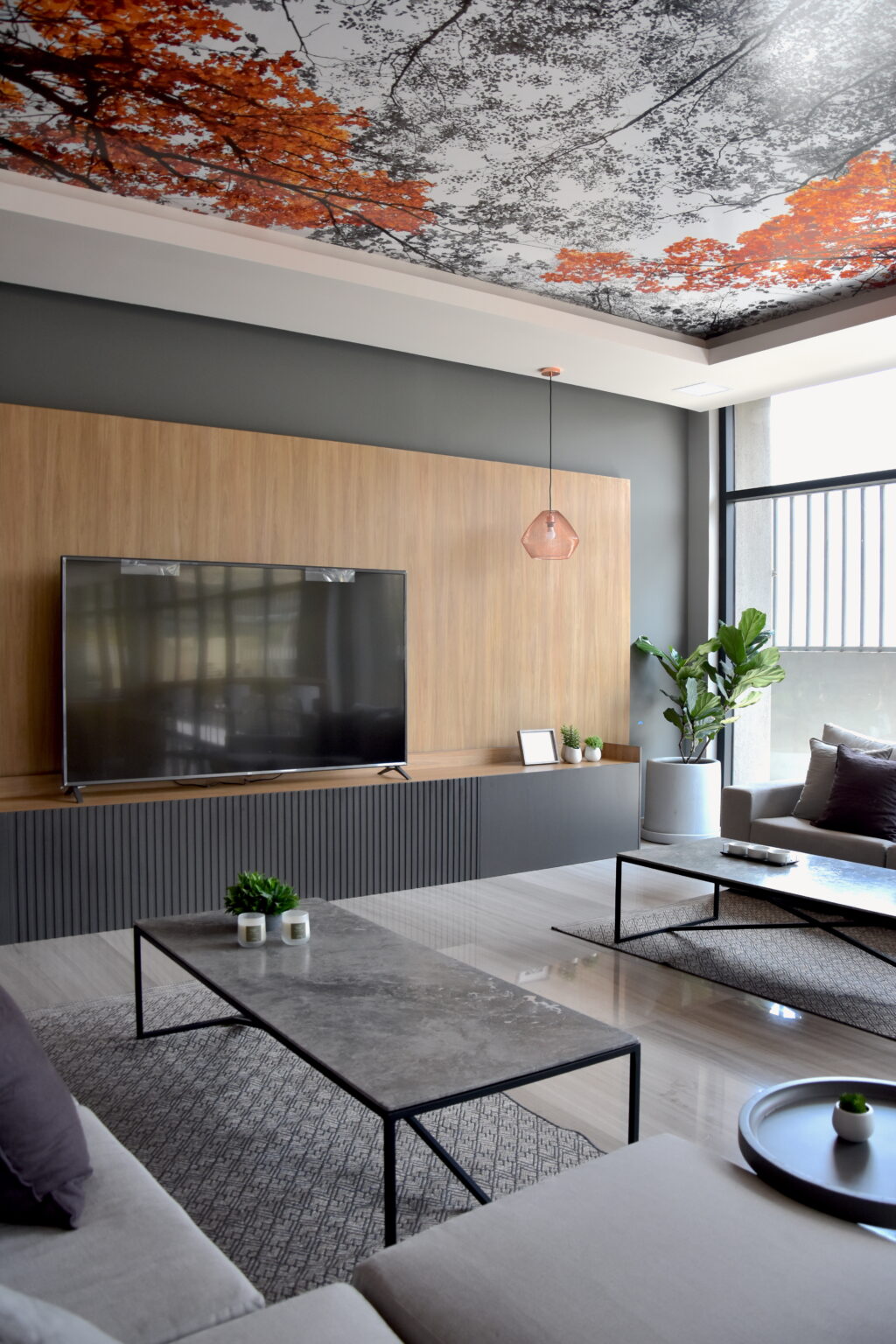 Sala de televisión con muro de madera, mesas de piedra y plafón con árboles