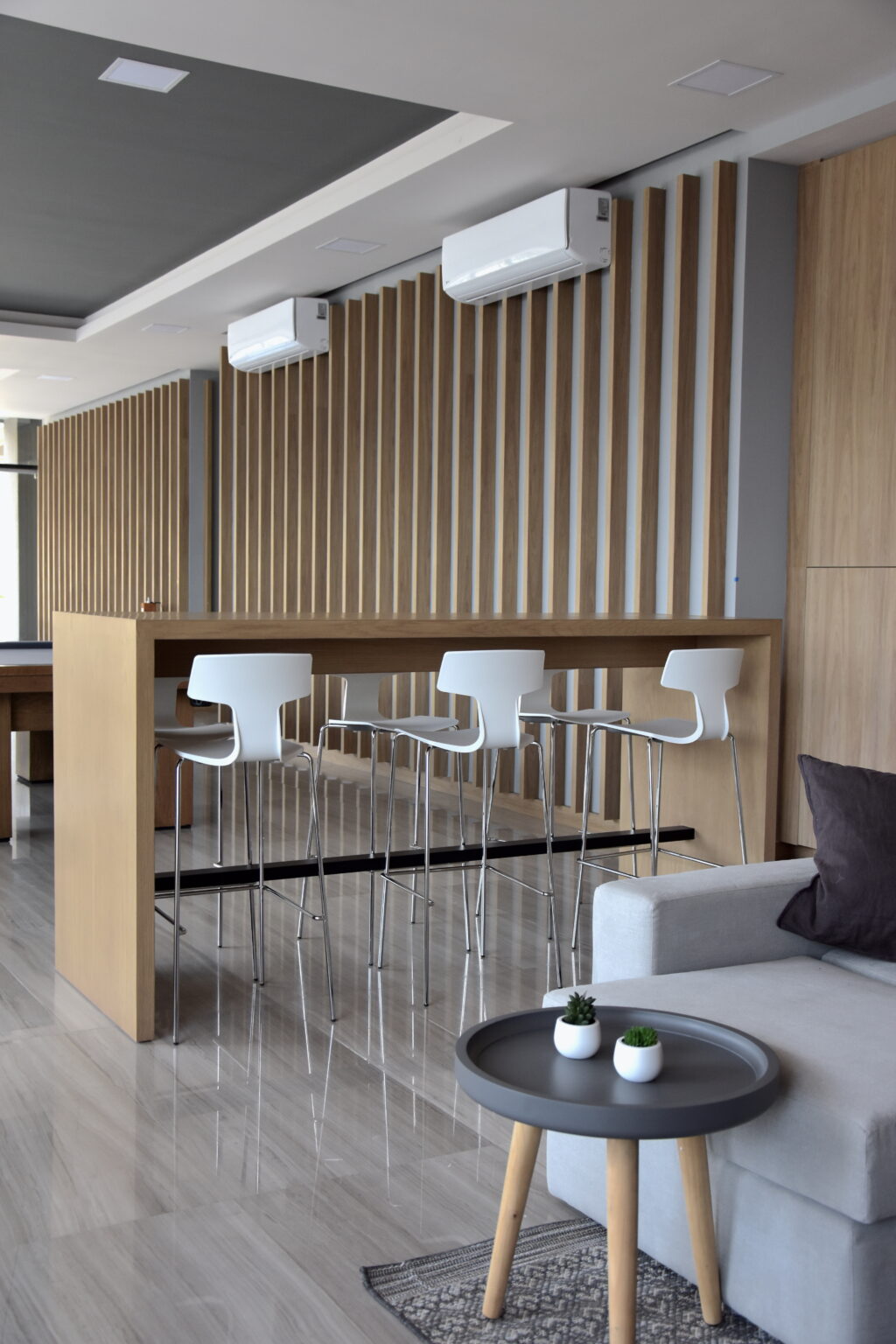 Barra alta de madera con bancos blancos y muro de listones verticales