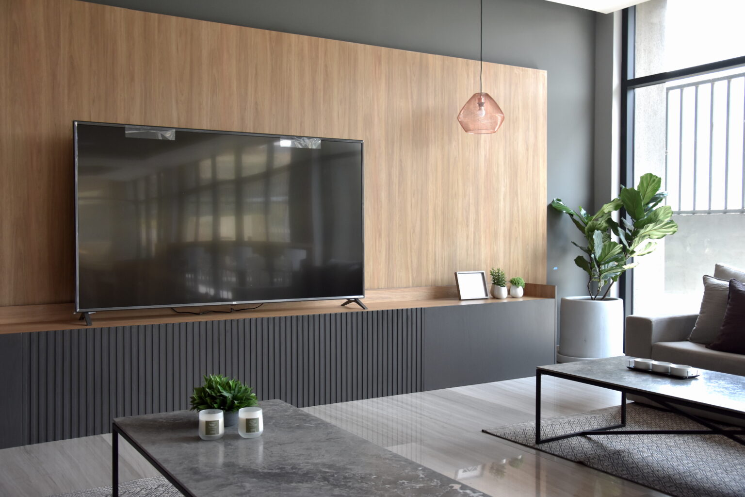 Televisión sobre mueble gris acanalado y panel de madera en la sala Borgó