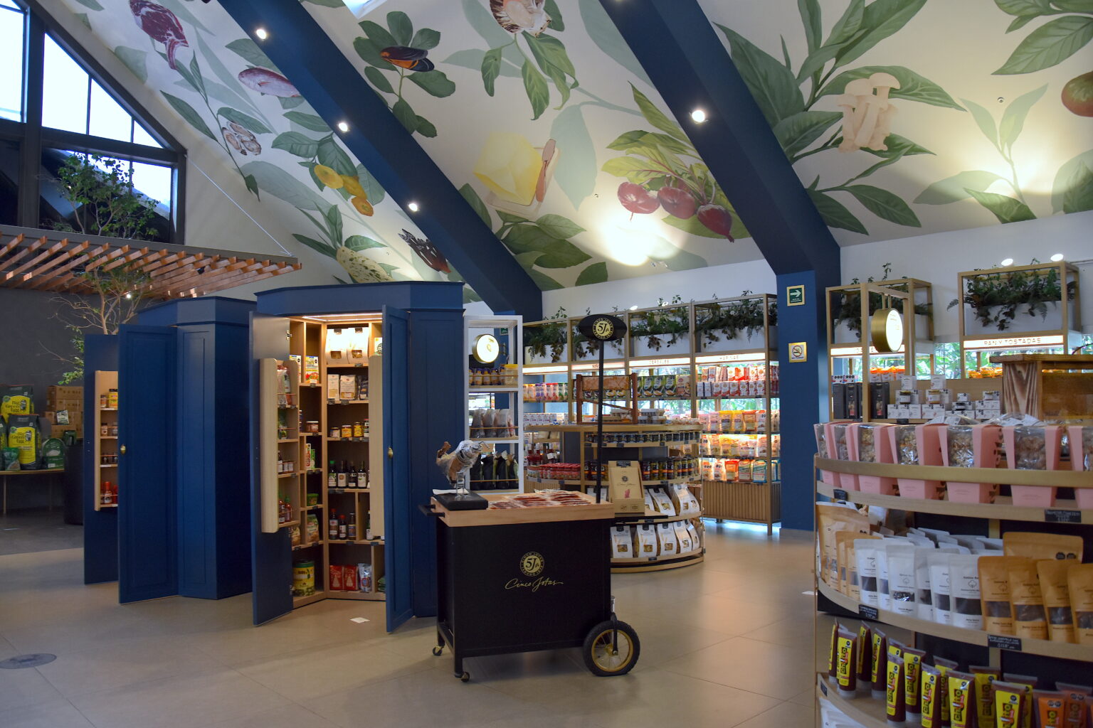 Exhibidores y gabinetes azules bajo el mural de ingredientes en Ingredienta Pedregal
