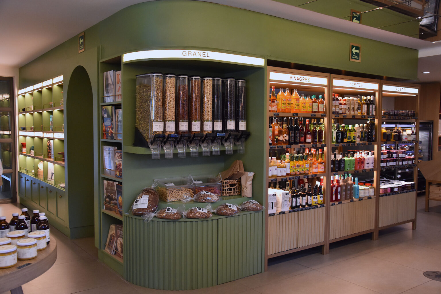 Mueble verde con dispensadores a granel y estantes de vinagres en Ingredienta Pedregal