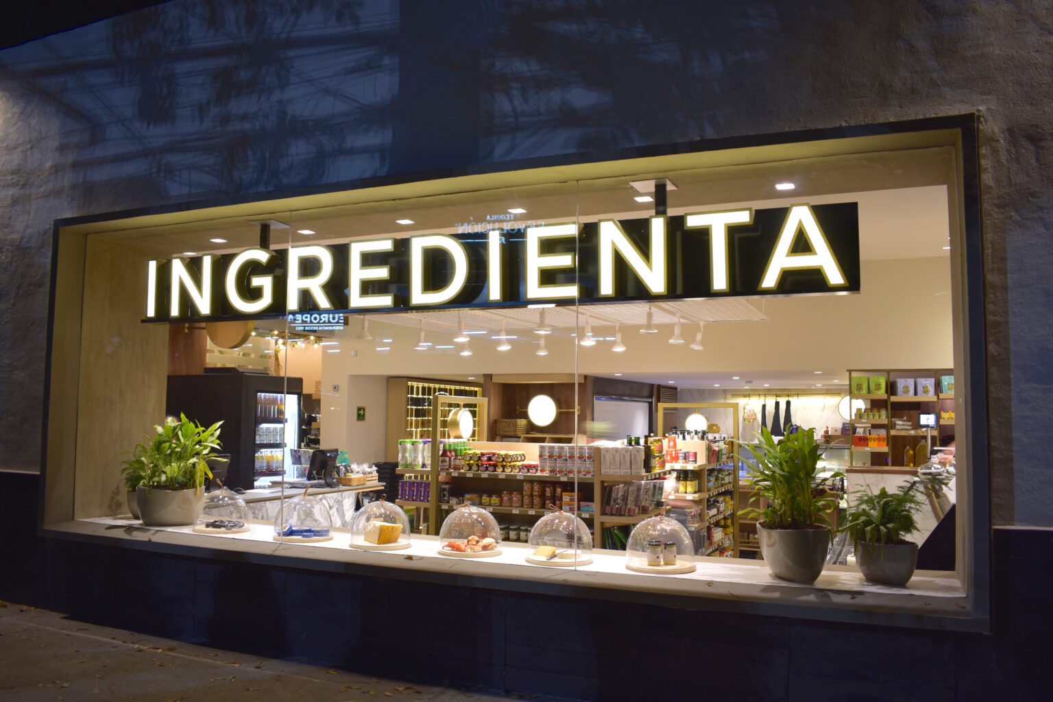 Fachada iluminada de Ingredienta Prado Norte con escaparate de productos gourmet