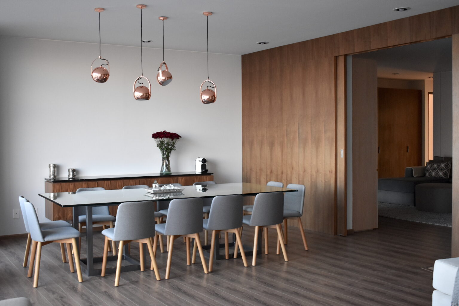 Comedor con mesa de cristal, sillas grises y lámparas colgantes de cobre en Lo Alto