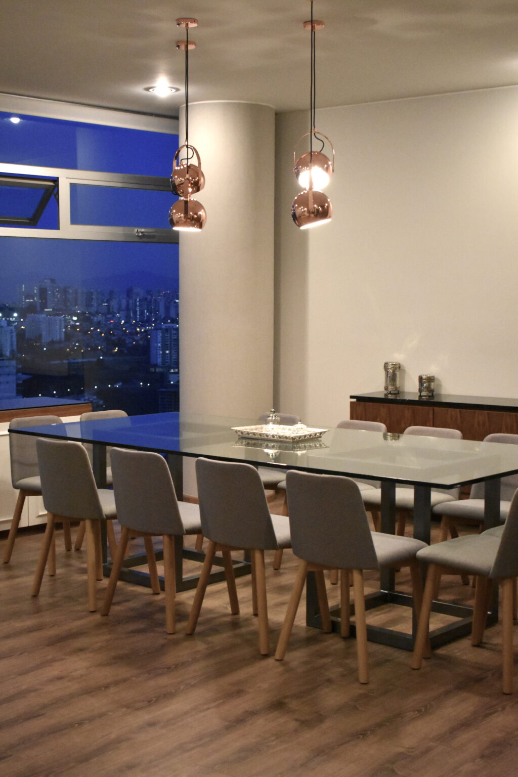 Comedor iluminado con lámparas de cobre y vista nocturna desde Bosque Real