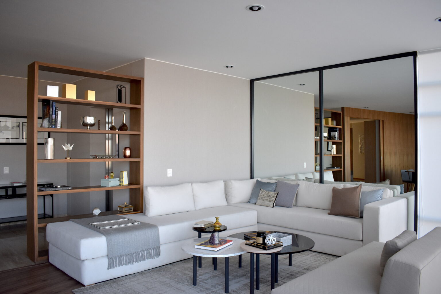 Sala principal con sofá seccional blanco, librero de madera y muro de espejo