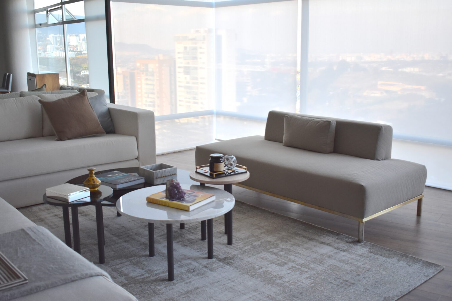 Sala con sofá gris, mesas redondas y ventanales panorámicos en la residencia Lo Alto