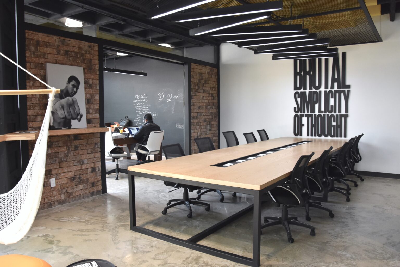 Sala de juntas con mesa larga de madera, muros de ladrillo y tipografía mural