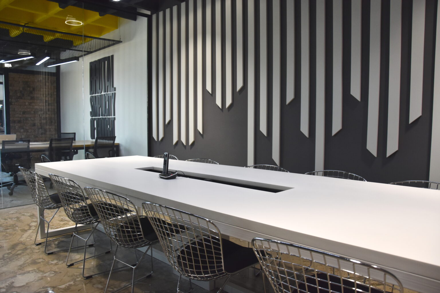 Sala de reunión con mesa blanca, sillas metálicas y muro gráfico blanco y negro