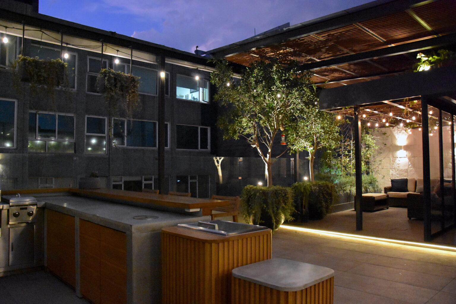 Vista nocturna de cocina exterior y pérgola iluminada en Roof Taine