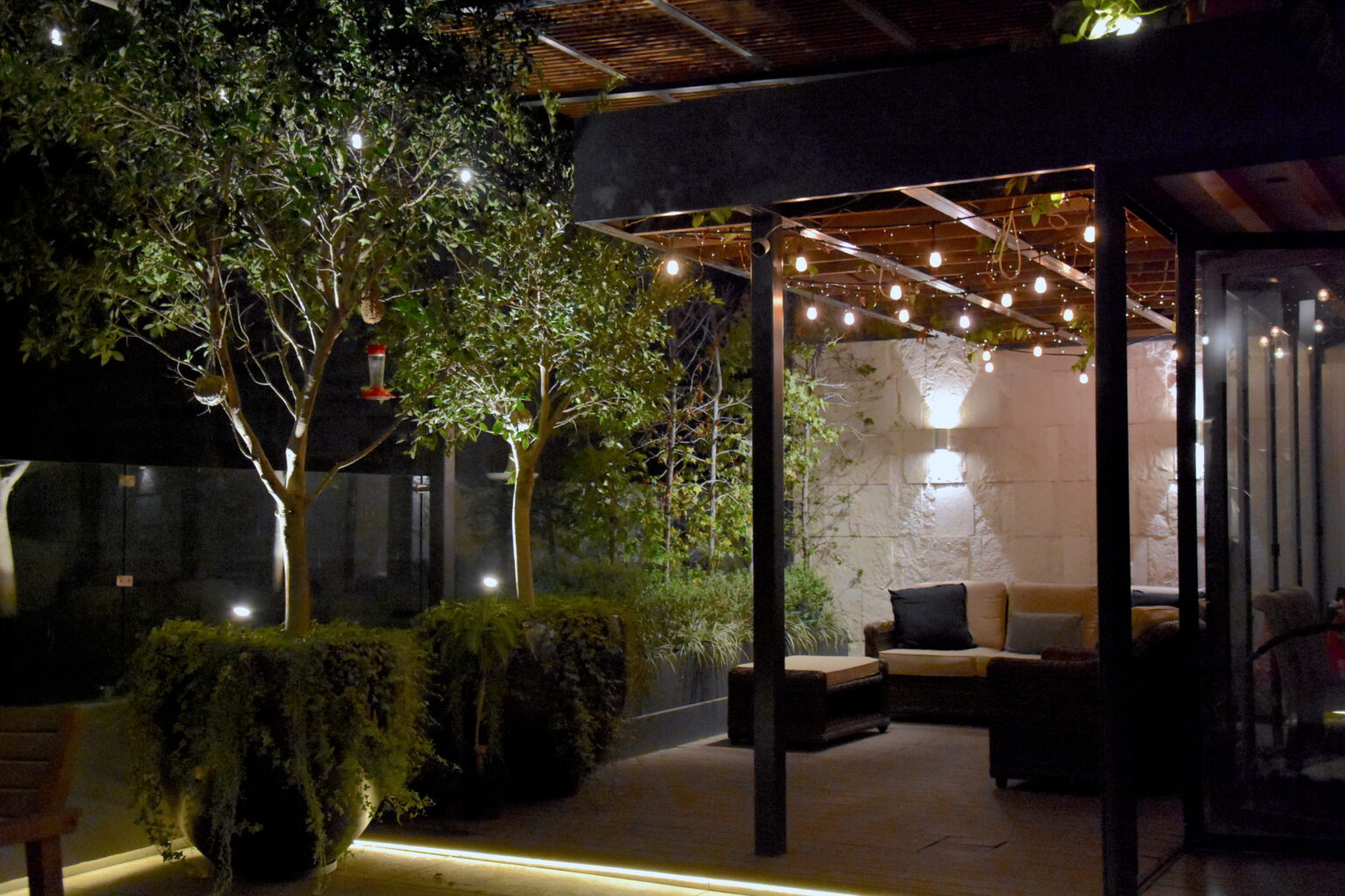 Sala exterior bajo pérgola con jardín e iluminación cálida en Roof Taine