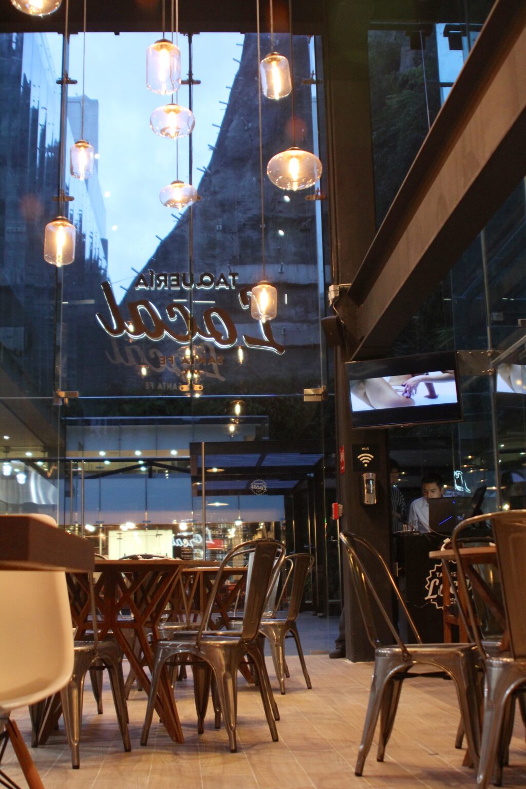 Interior del comedor con lámparas colgantes y logotipo de Taquería Local