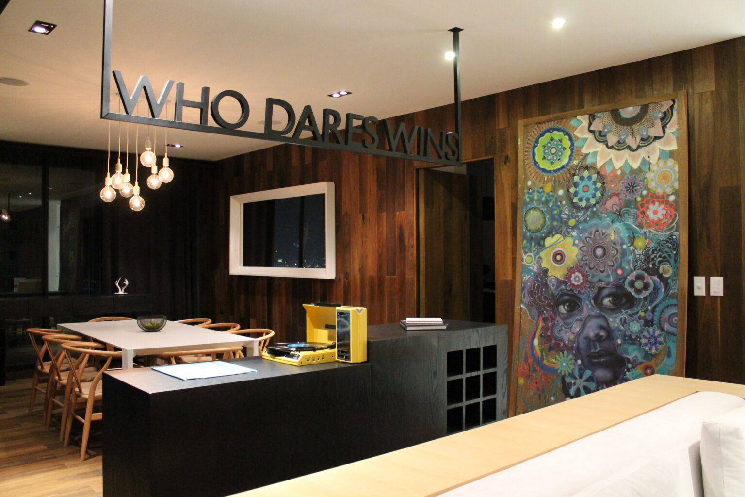 Área social de Avivia con comedor, sofá blanco, mural colorido y mobiliario negro