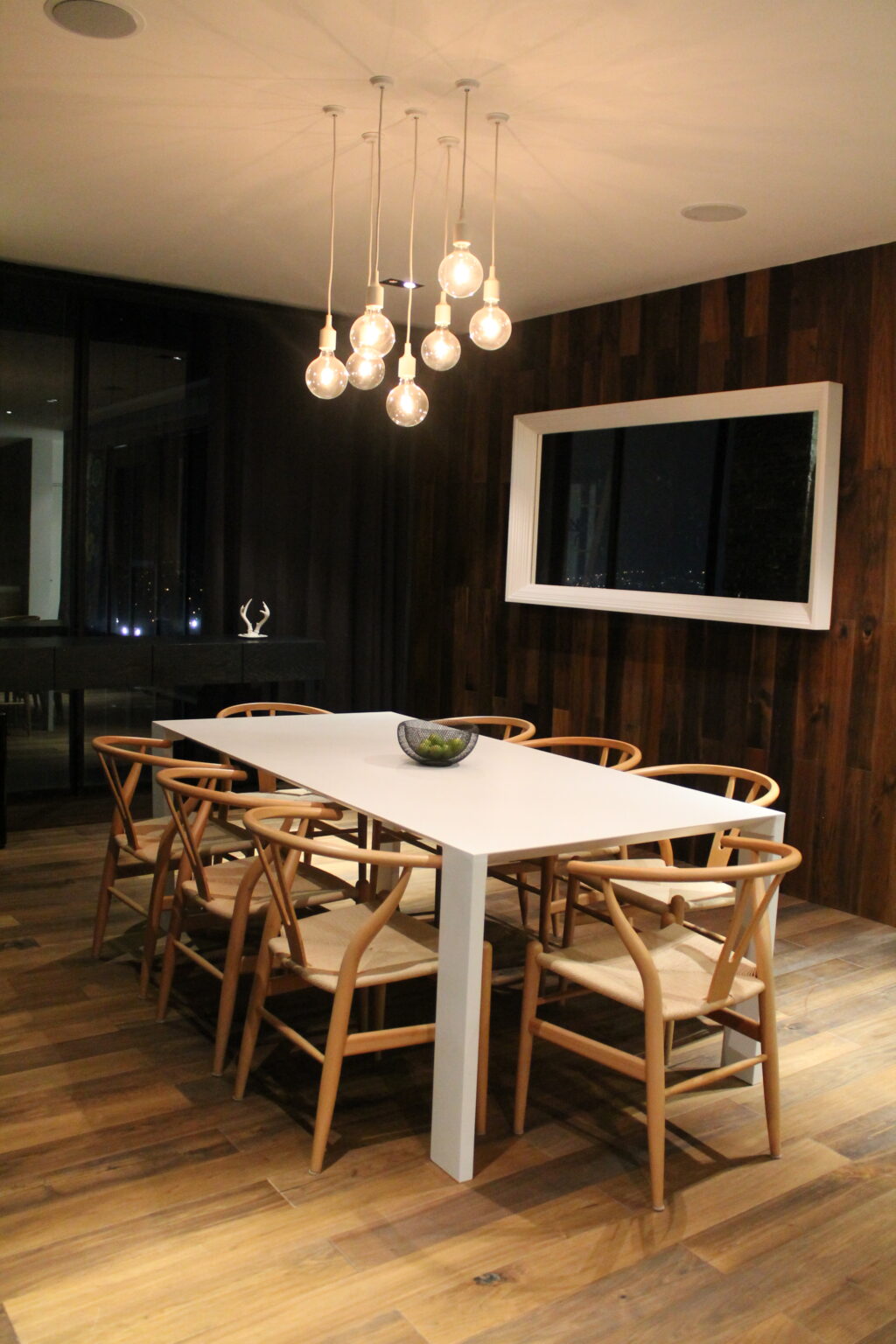 Comedor de Avivia con mesa blanca, ocho sillas de madera y lámparas de vidrio