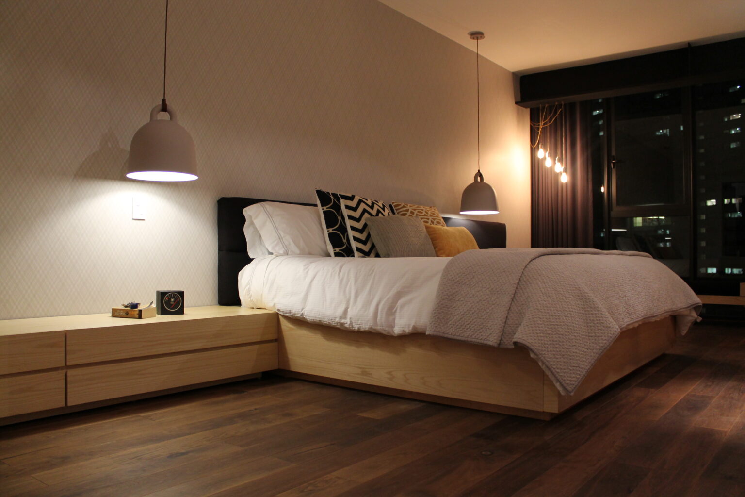 Recámara principal nocturna de Avivia con cama de madera y lámparas colgantes