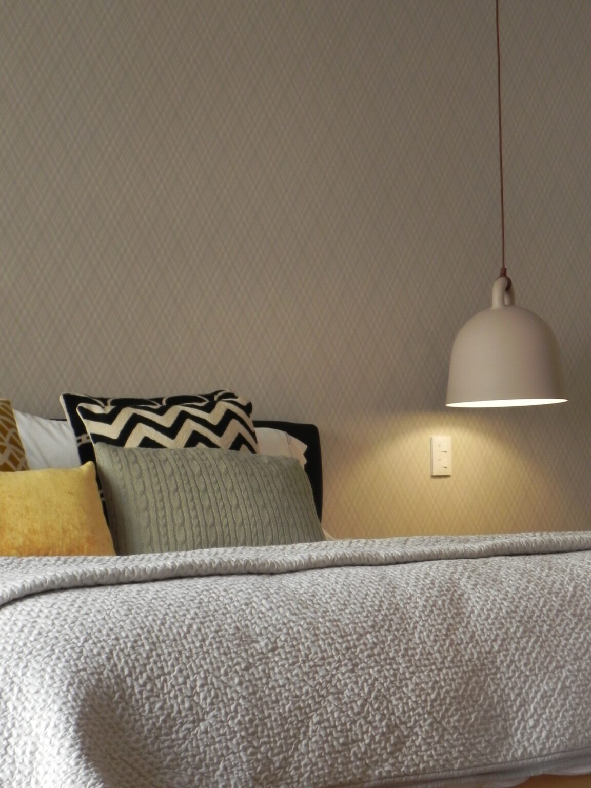 Detalle de cama con textiles tejidos y lámpara colgante en la recámara de Avivia