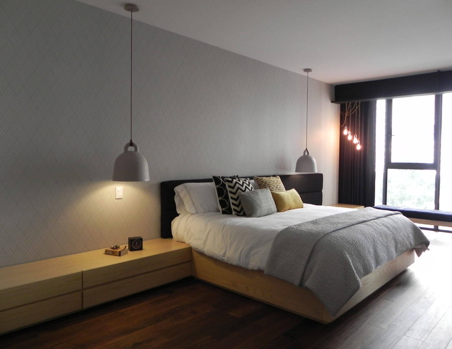 Recámara principal de Avivia con cama de madera, buró corrido y lámparas colgantes