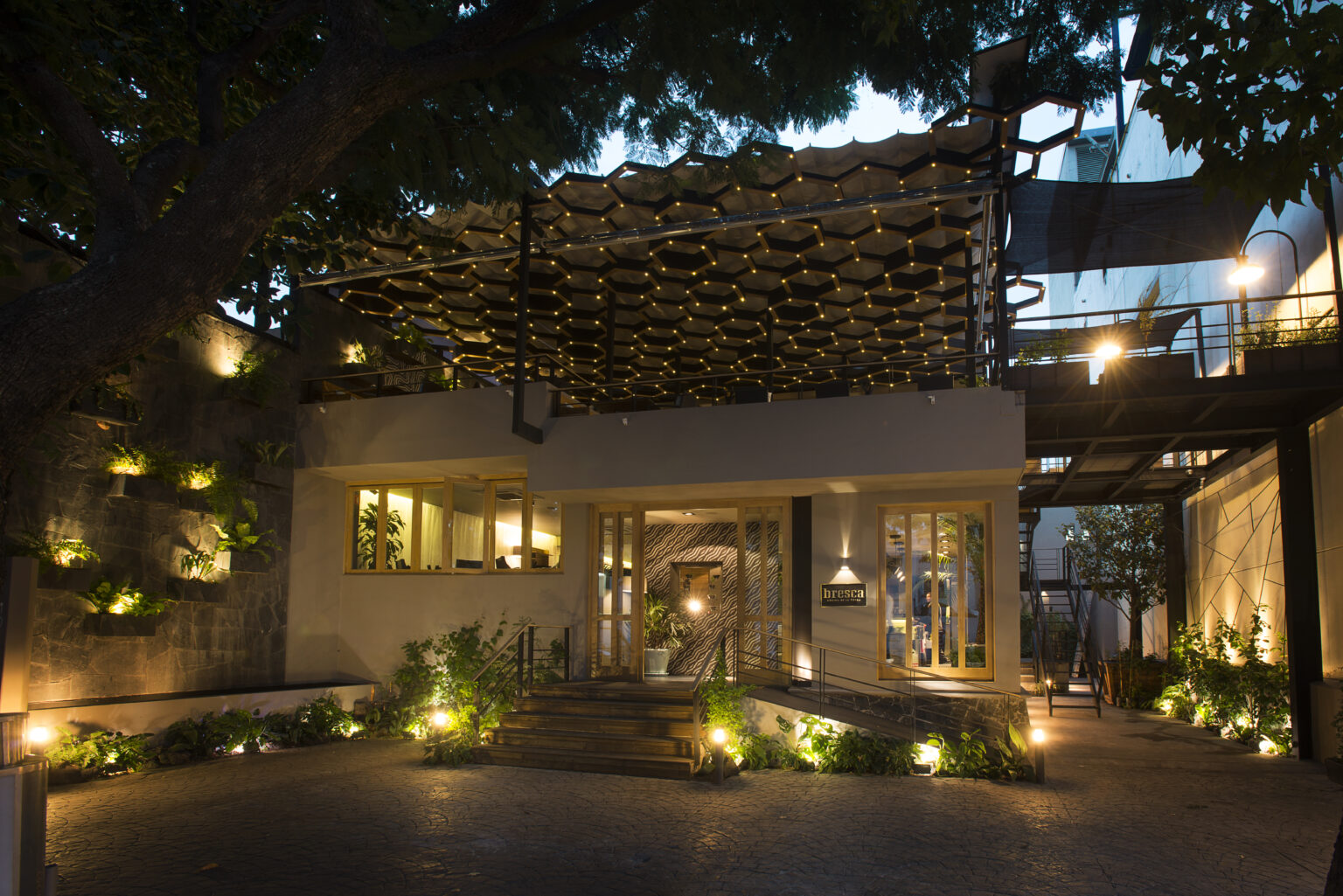 Fachada nocturna del restaurante Bresca con pérgola iluminada y acceso ajardinado