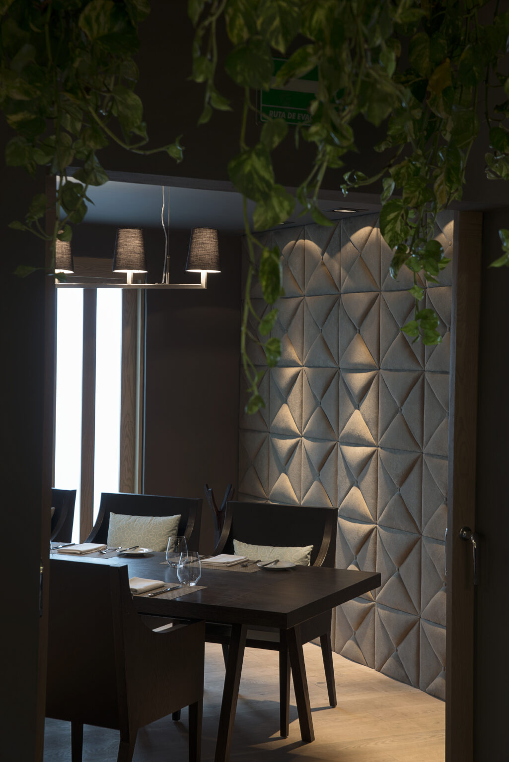 Comedor de Bresca con mesa de madera y muro acolchado de paneles geométricos
