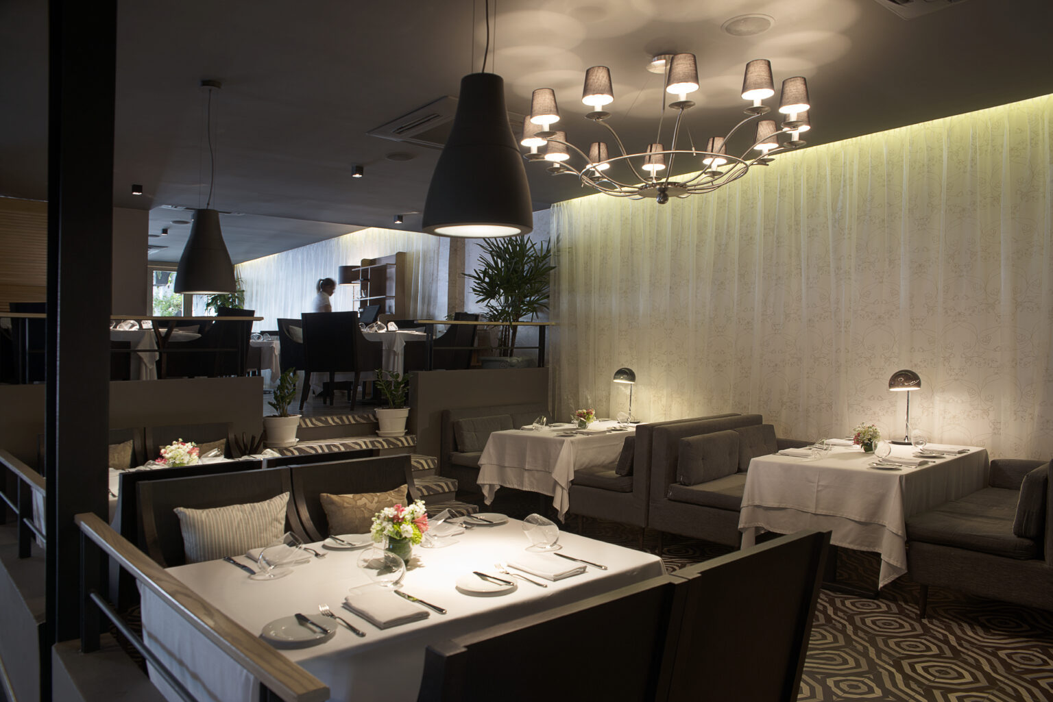 Comedor de Bresca con mesas vestidas, bancas grises y lámpara decorativa central