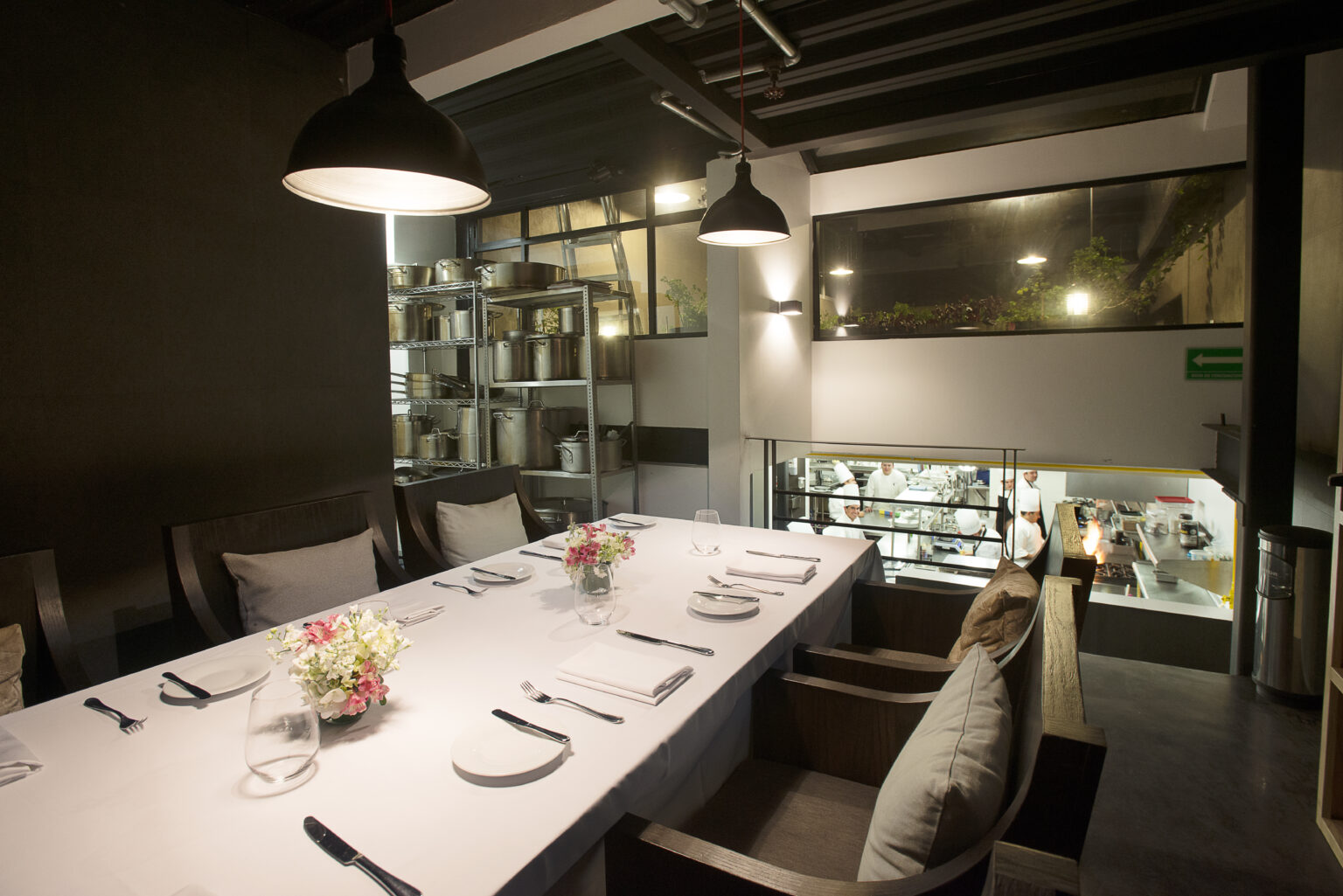 Mesa de comedor de Bresca frente a la cocina abierta con lámparas negras