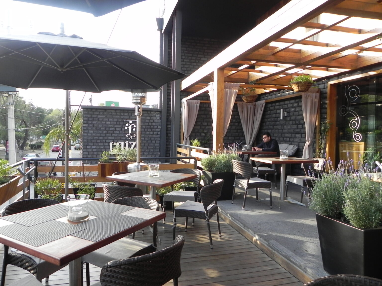 Terraza exterior de Raíz con mesas, sombrillas, jardineras y pérgola de madera