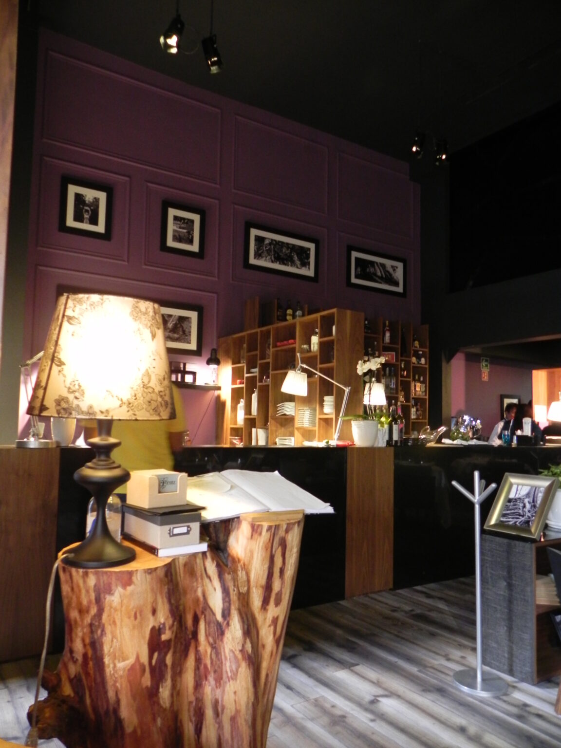 Recepción del restaurante Raíz con mueble de tronco, lámpara y muro morado