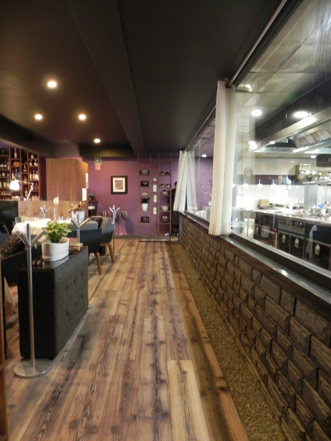 Pasillo del comedor junto a cocina abierta con cristal y muro de ladrillo en Raíz