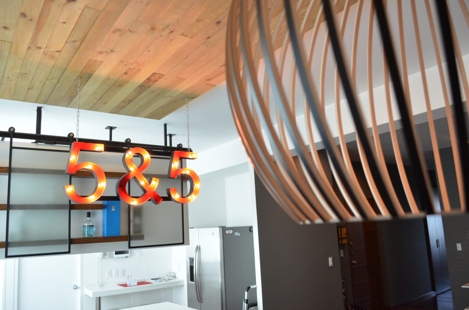 Bar suspendido con letrero luminoso 5&5, plafón de madera y luminaria escultórica