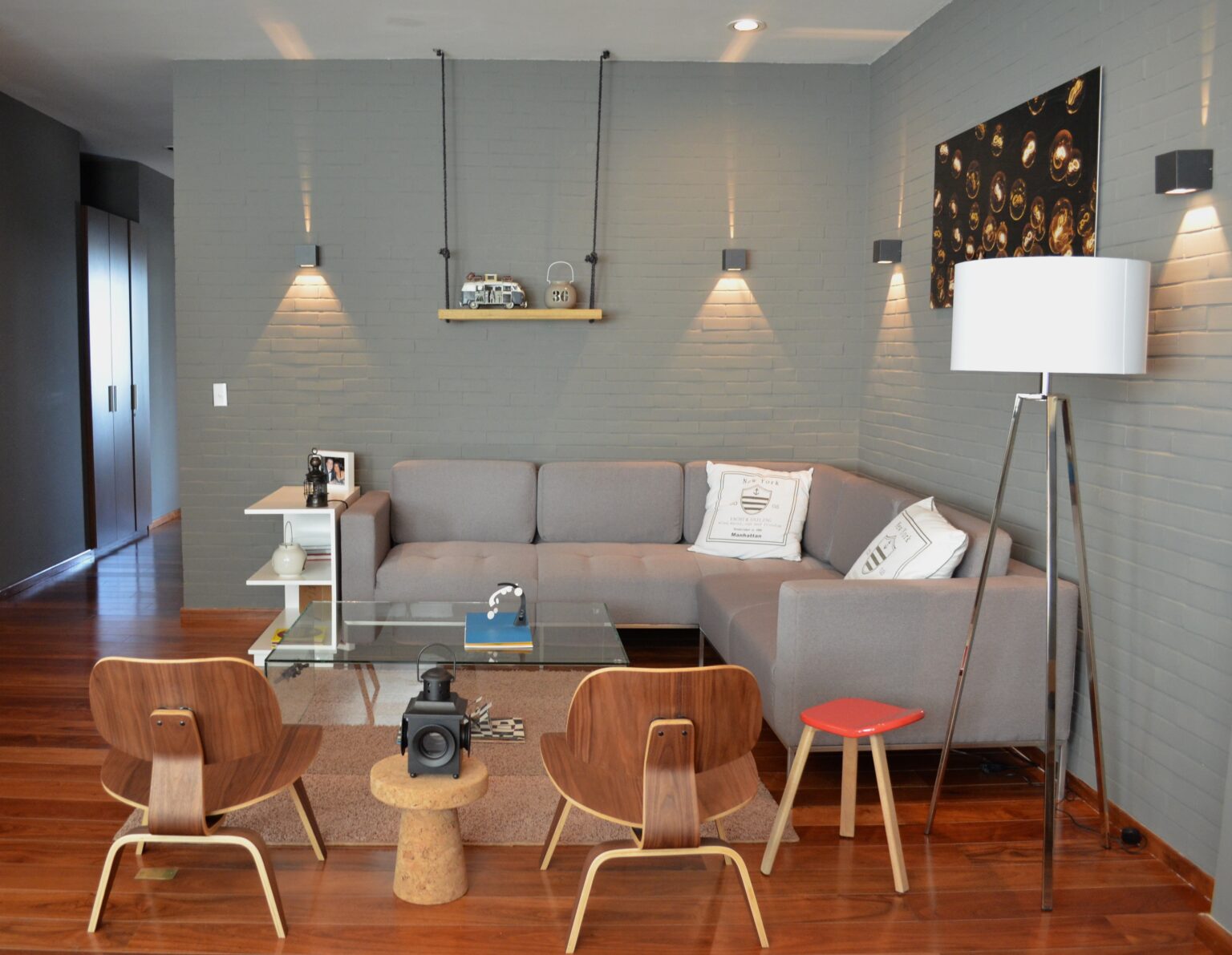 Sala con sofá seccional gris, sillones de madera y mesa de centro de cristal
