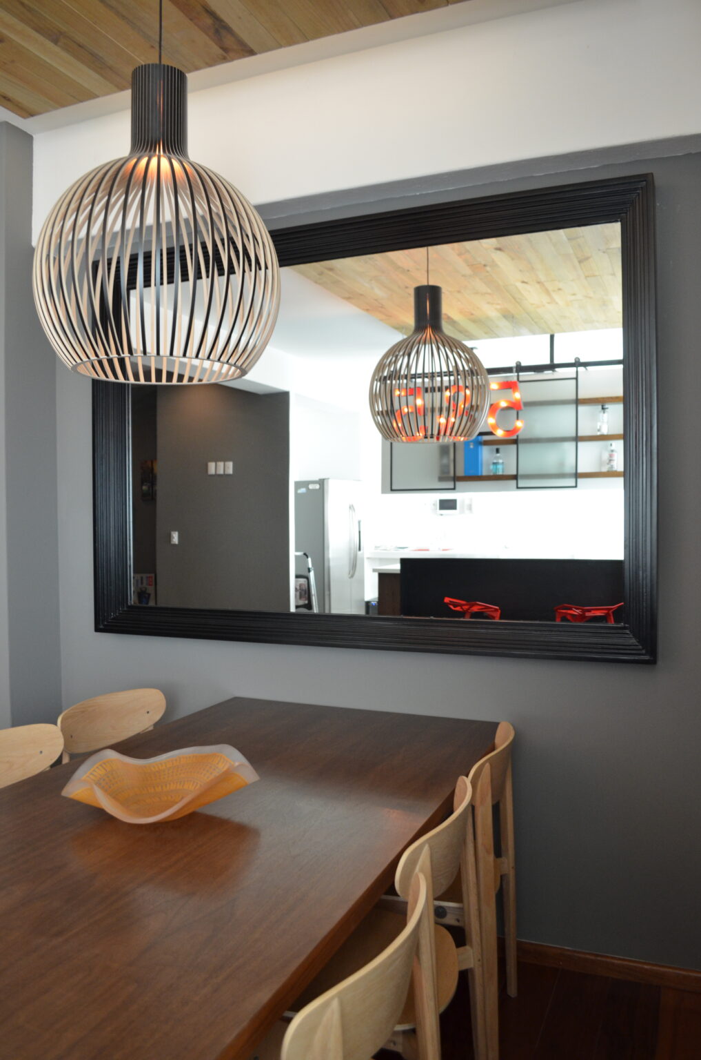Mesa de comedor y lámpara de varillas frente a espejo que refleja la cocina