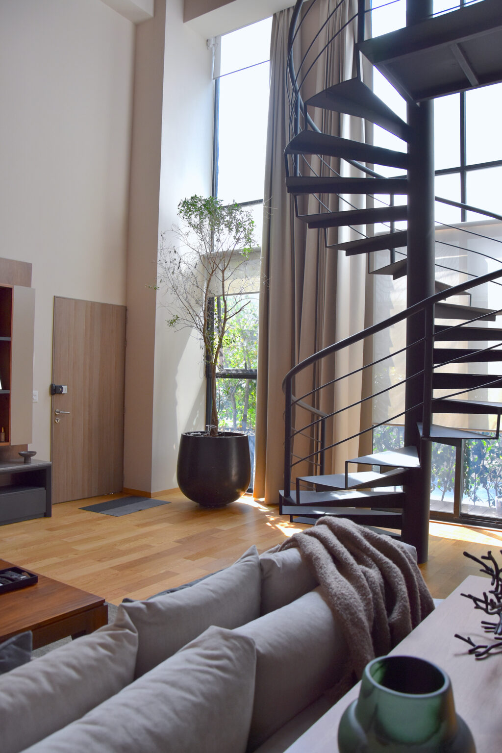 Escalera helicoidal negra junto a ventanales de doble altura y sala de Casa Roma