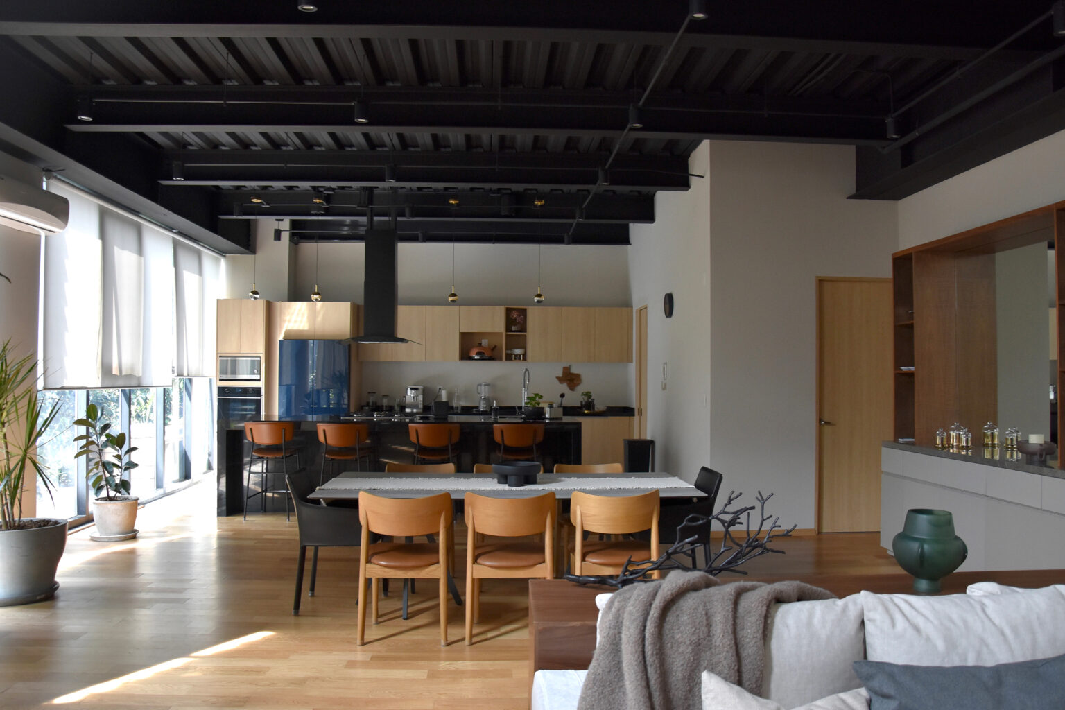 Cocina abierta con isla negra, sillas color cuero y comedor de madera en Casa Roma