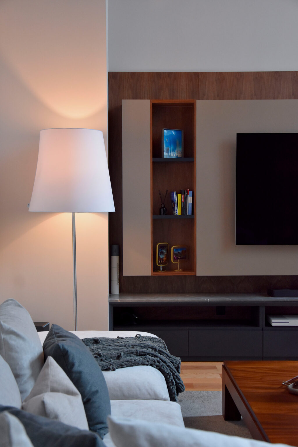 Mueble de televisión con nichos de madera, gabinetes grises y lámpara de piso