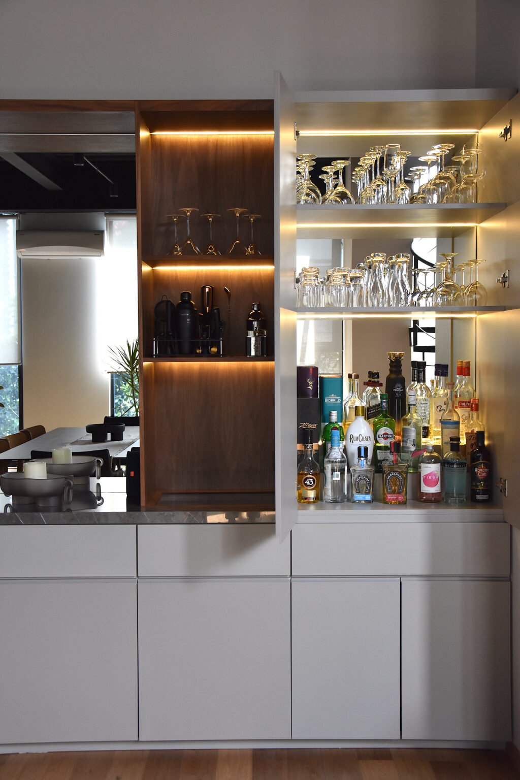 Bar empotrado con botellas, cristalería, repisas iluminadas y espejo en Casa Roma